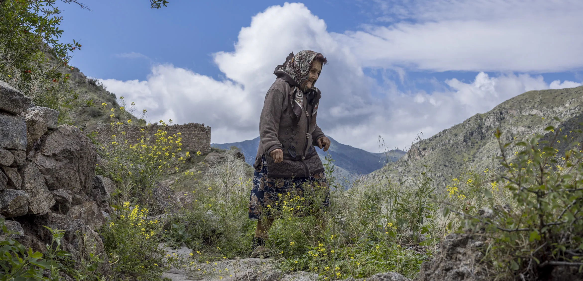 An elderly woman walks along a stone mountain path in Armenia, part of the Danish Cultural Institute's Landscapes of Memories project.